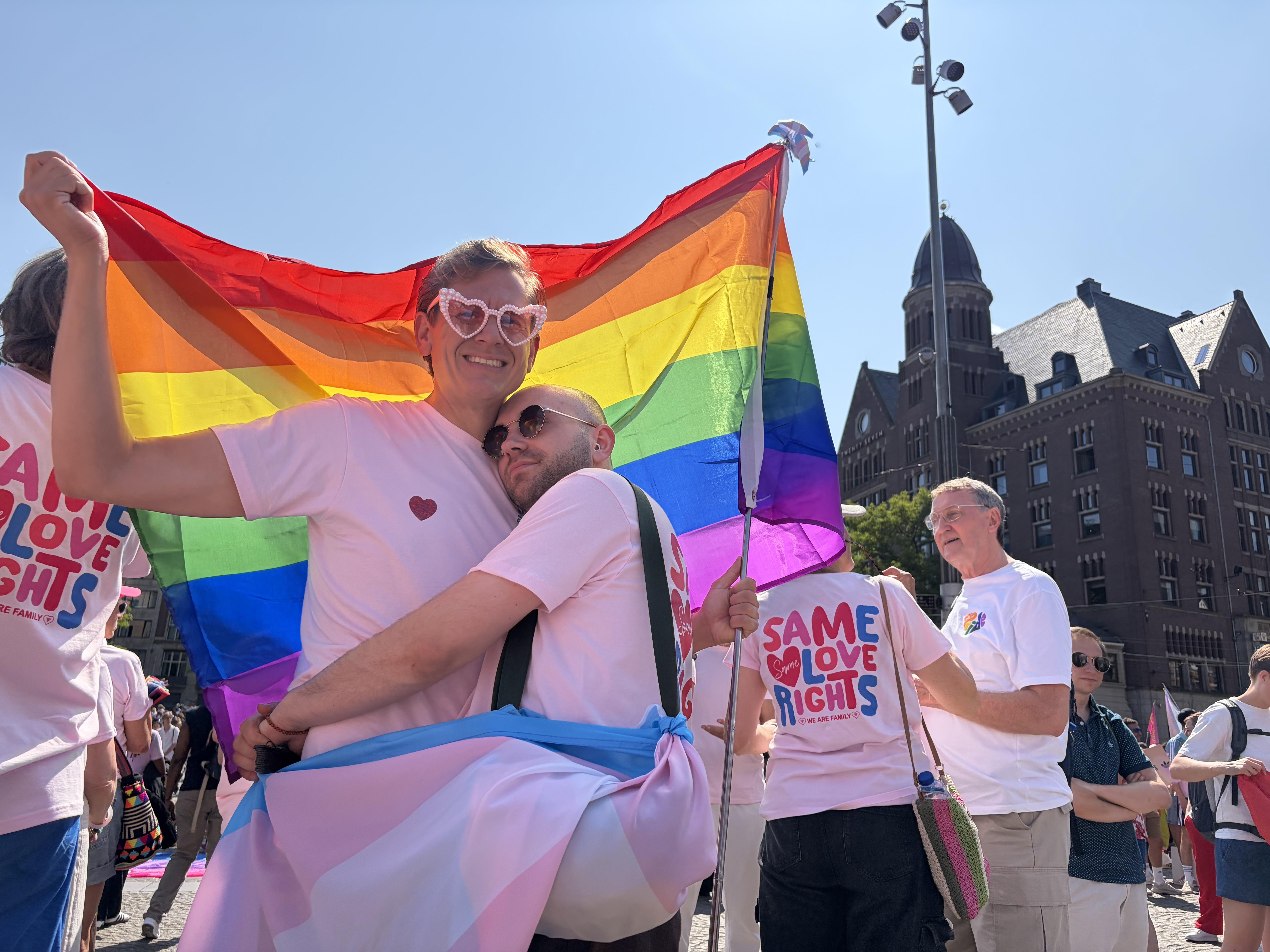 a lovely couple holds each other and holding a pride flag in Dams Square Amsterdam