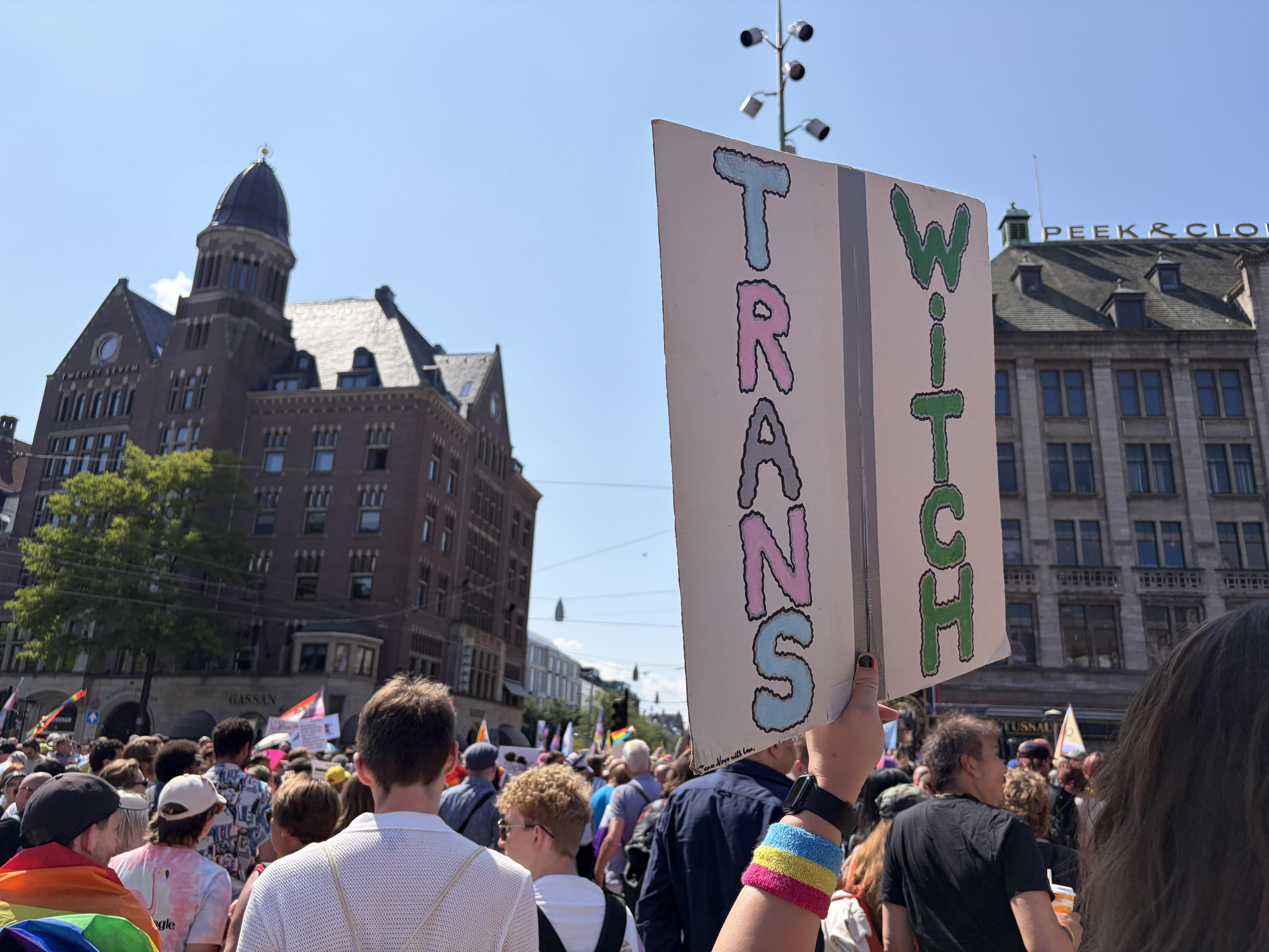 Trans Witch sign with a big crowd of people going to the Pride Walk from Dams Square Amsterdam