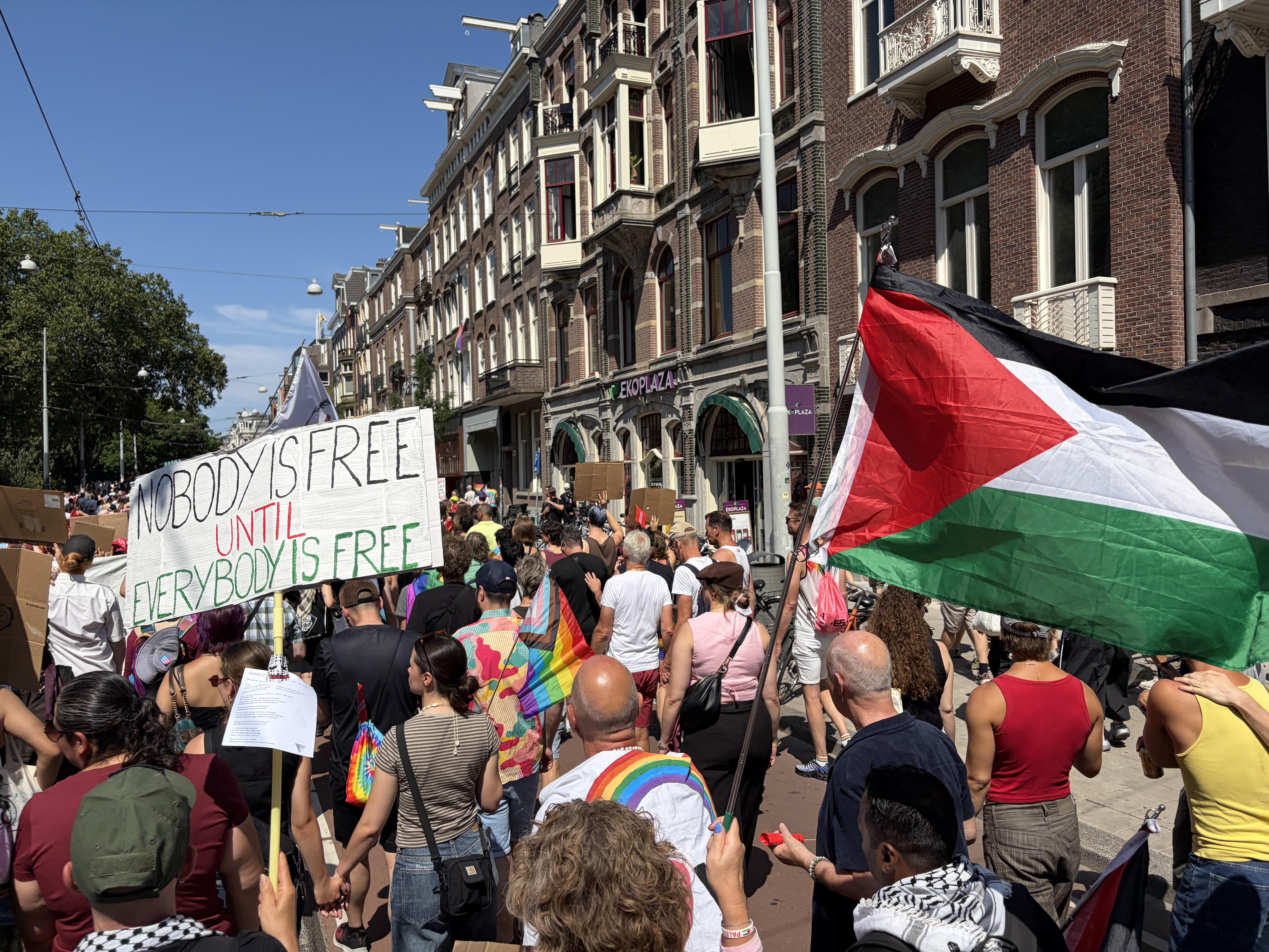Pride Walk Amsterdam, sign reads "nobody is free until everybody's free" next to a Palestinian flag