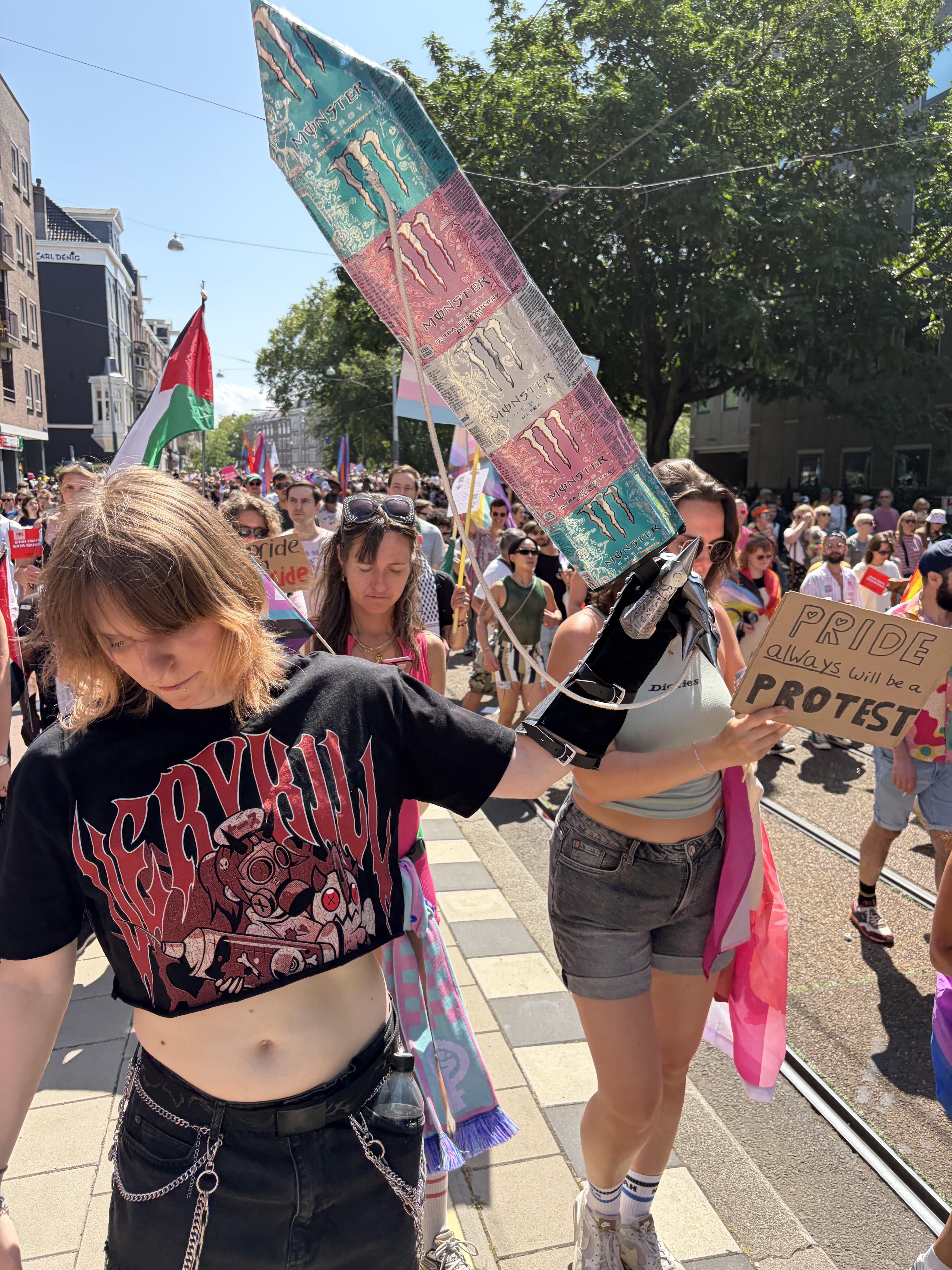 "Pride always will be a protest" sign next to a massive Monster sword, Pride Walk Amsterdam