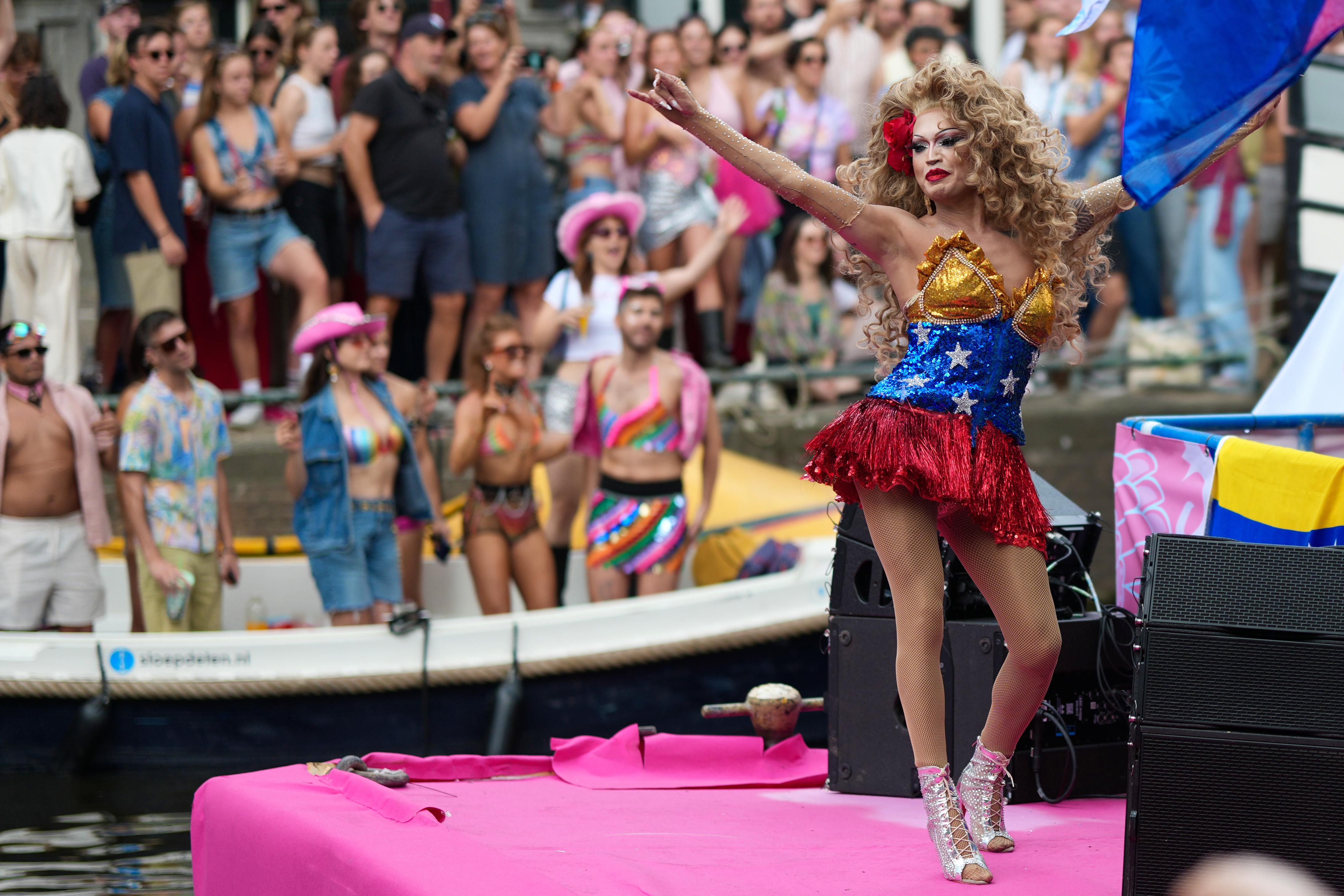 a fabulous drag queen dances on the front of a boat at Canal Pride in Amsterdam, many people cheering in the background
