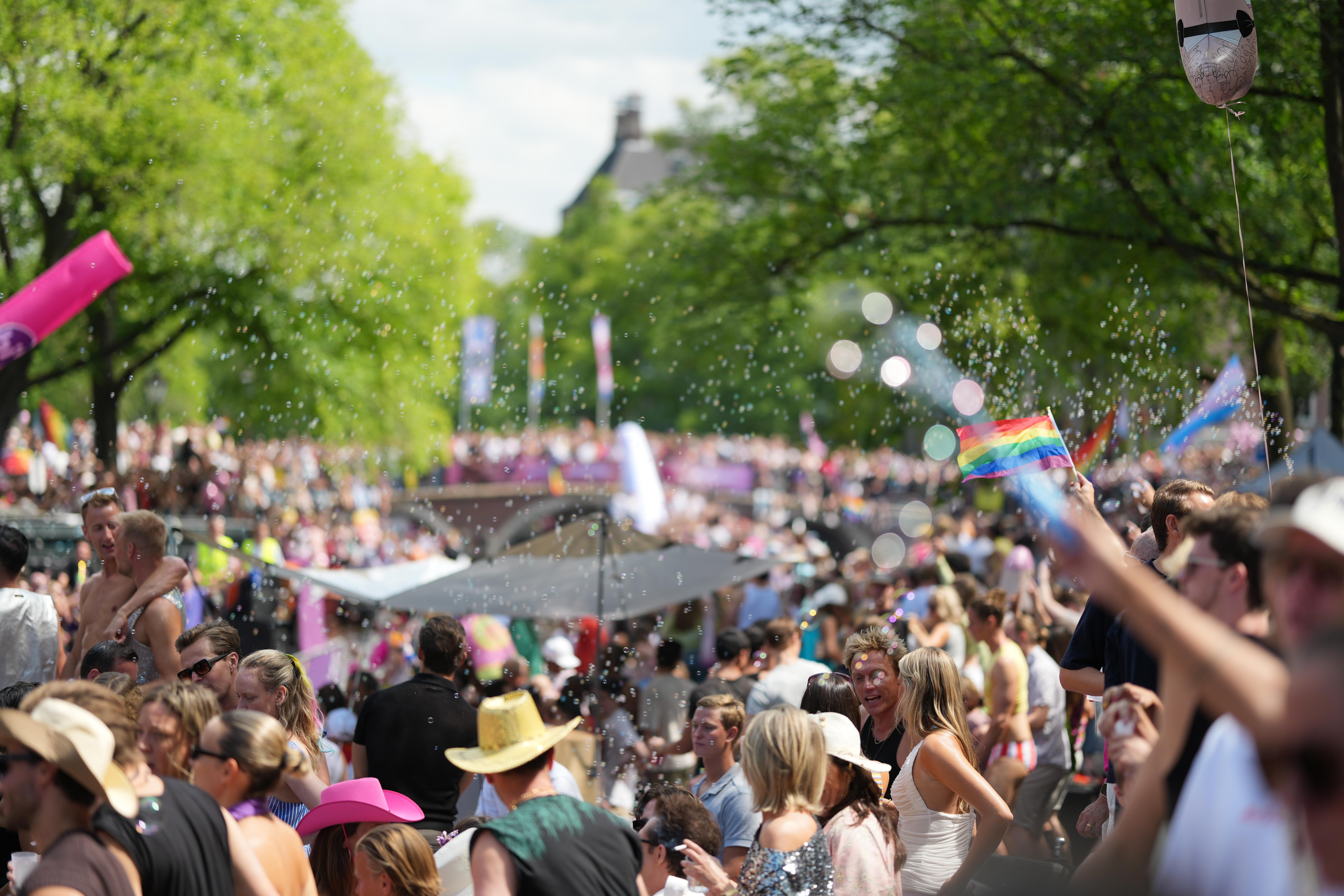 a dreamy scene of thousands of people with bubble blowing through the wind as they dance, cheer, and watch Canal pride in Amsterdam