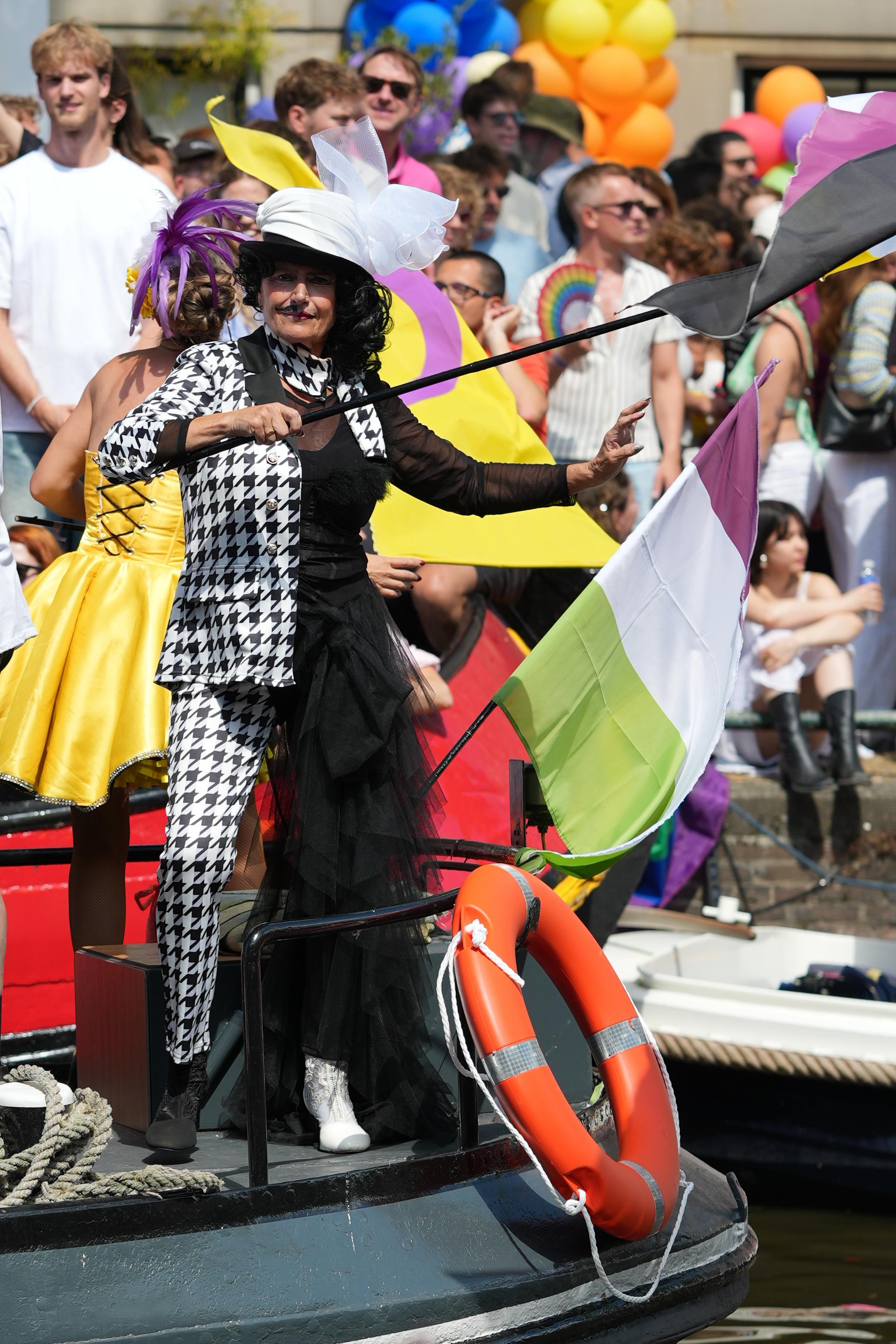 a well dressed person dances and waves a pride flag on a boat at Canal Pride in Amsterdam