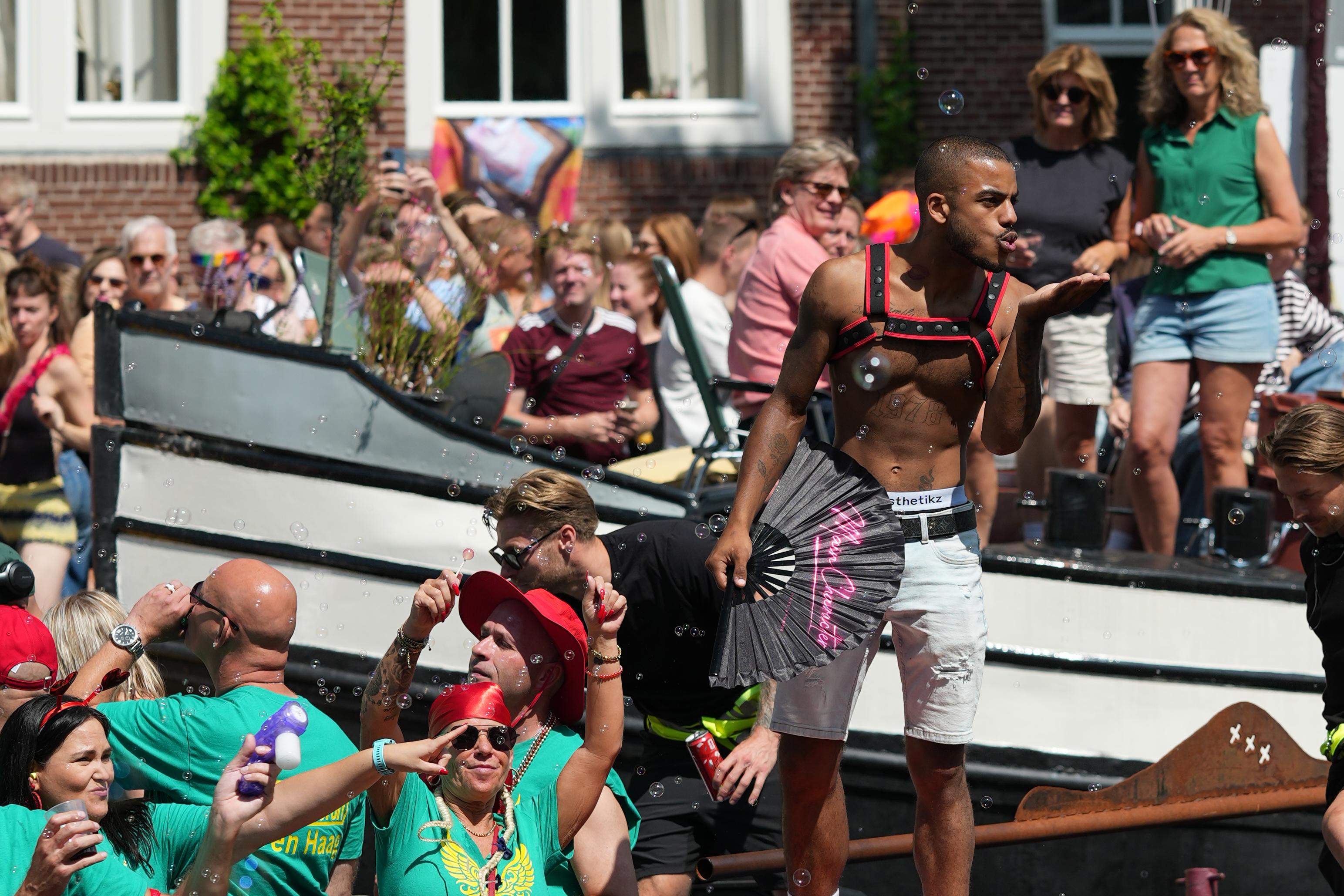 a striking guy either blowing a kiss or blowing bubbles, and bubbles from bubble guns fly around him, at Canal pride in Amsterdam