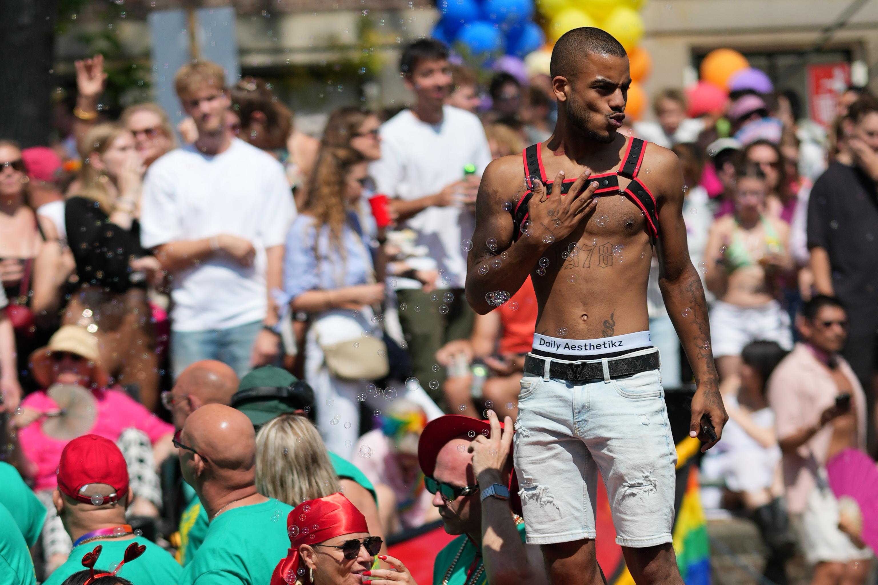 a striking guy posing as bubbles from bubble guns fly around him, at Canal pride in Amsterdam