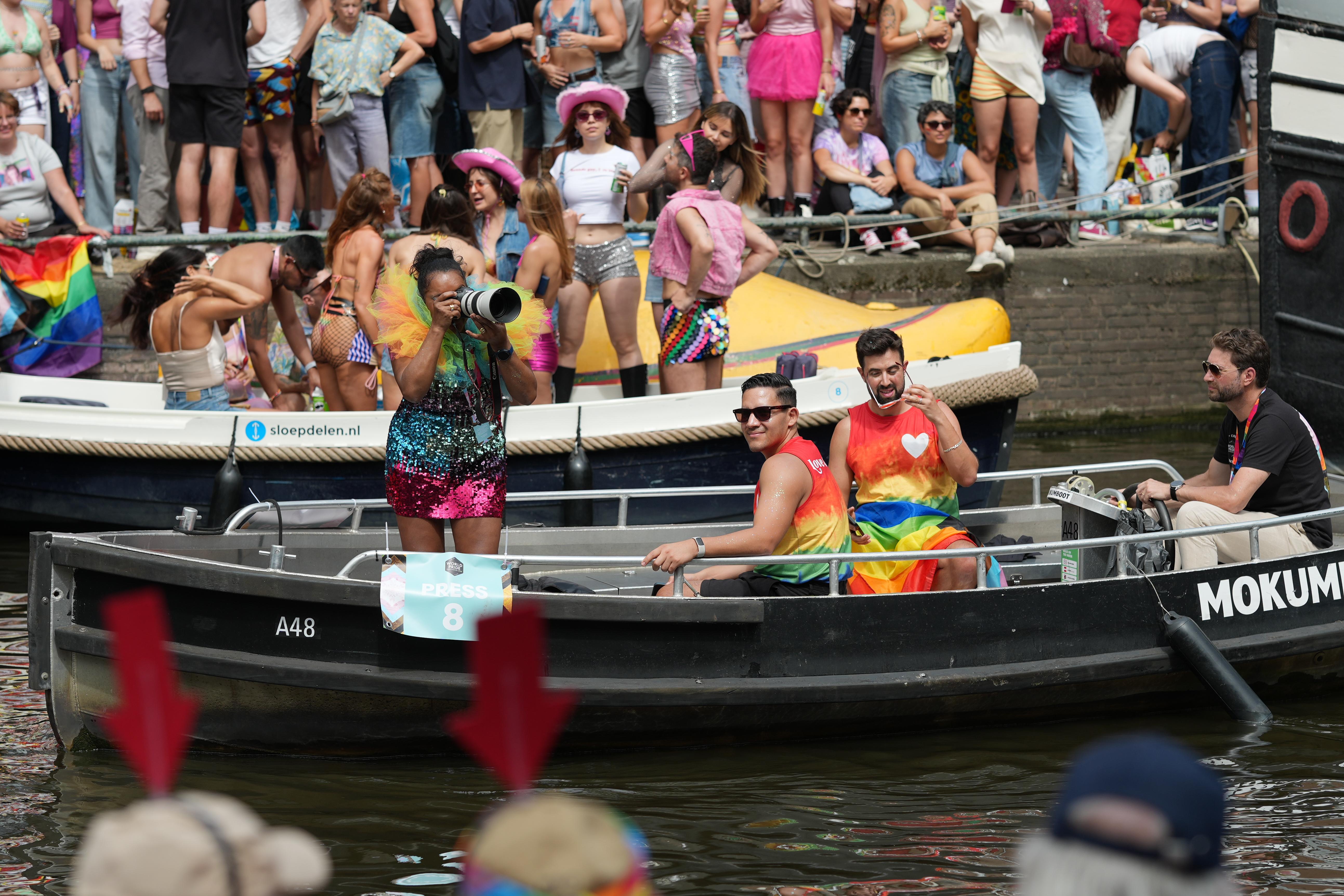 an event press photographer holds up her Cannon camera and takes pictures of the crowds, at Canal Pride in Amsterdam